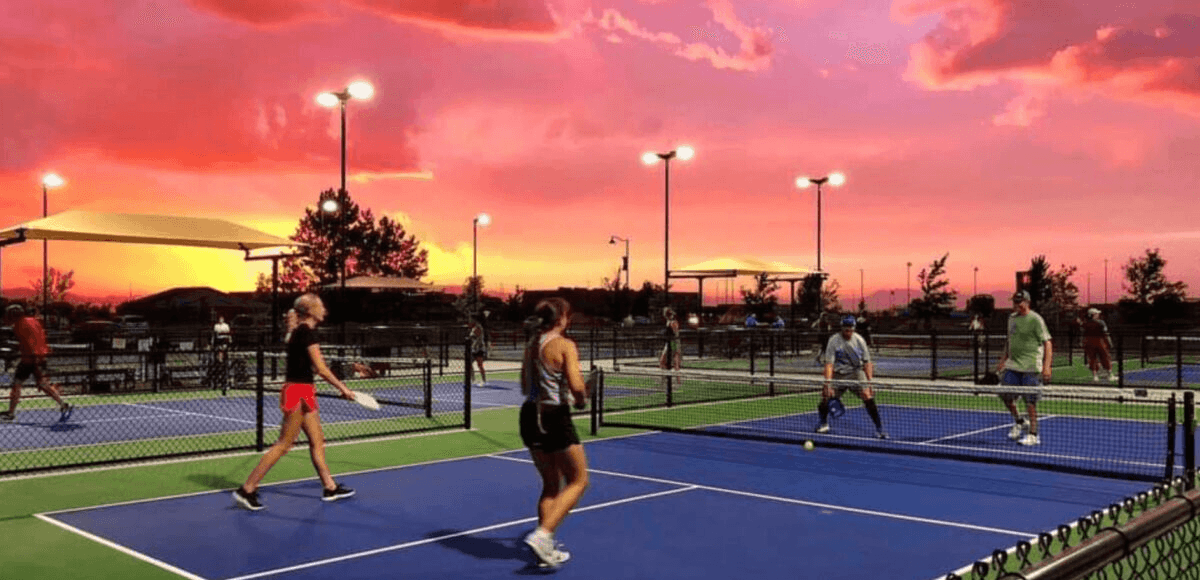 Pickleball players enjoying games during a beautiful sunset with dramatic pink and orange sky
