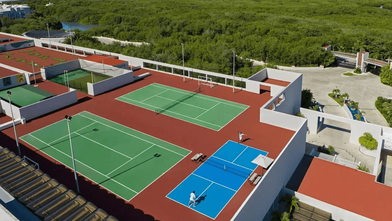Aerial view of a modern pickleball facility with multiple colorful courts surrounded by tropical vegetation